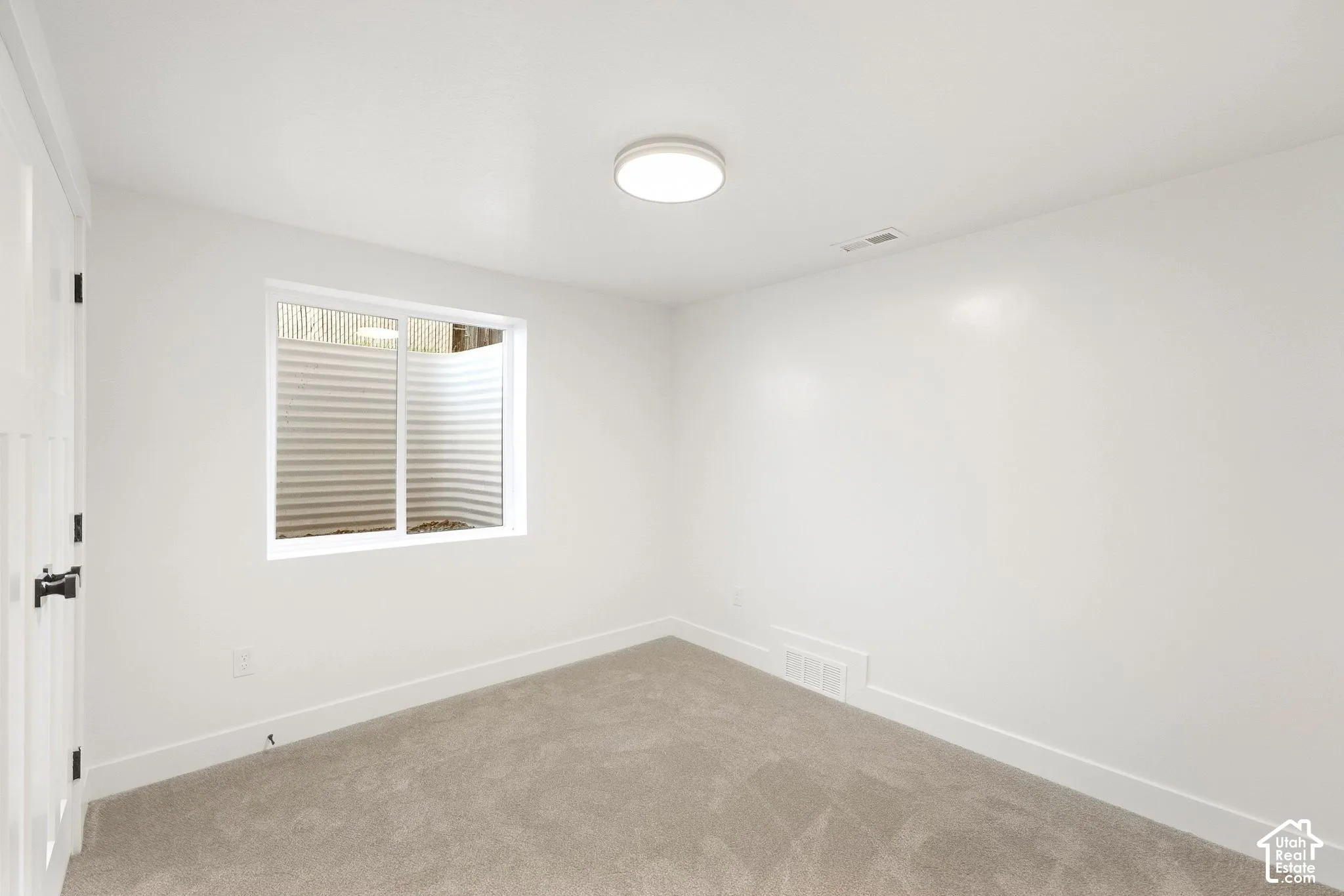 Neutral-toned carpet flooring, white walls, and a single window with a window well