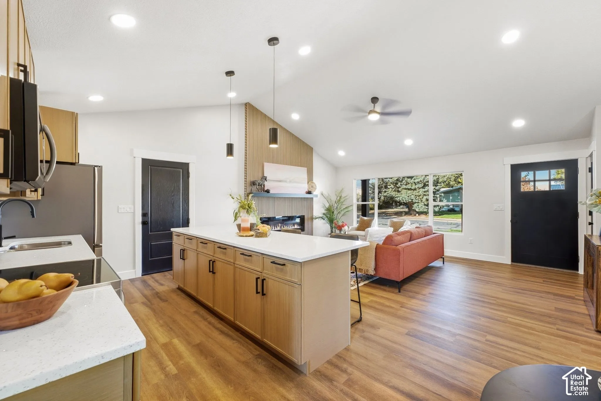 Vaulted ceilings with recessed lighting, large kitchen island with light cabinetry, wood-finish flooring, and a contemporary fireplace with a wood-slat accent wall