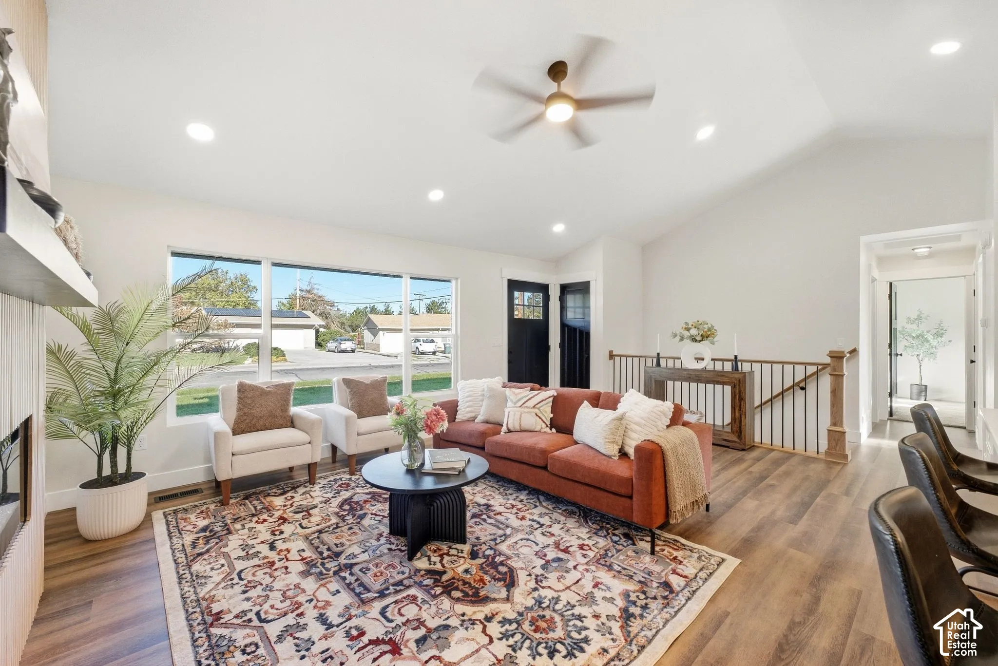 Vaulted ceiling with recessed lighting, wood-finish flooring, large picture window, and a wood and metal staircase