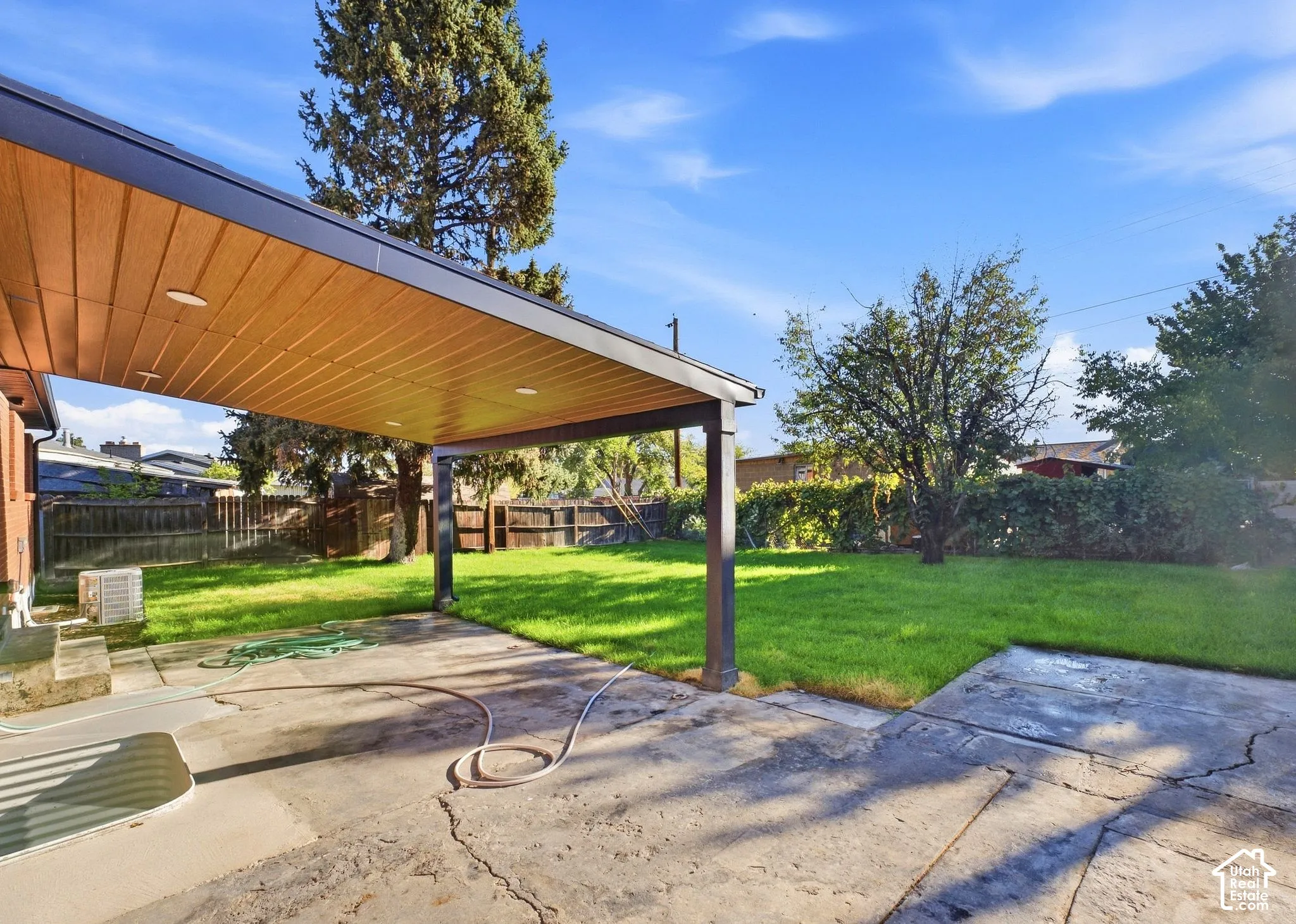 Expansive backyard featuring a covered patio with wood-finish ceiling and recessed lighting, concrete patio, and a grass lawn