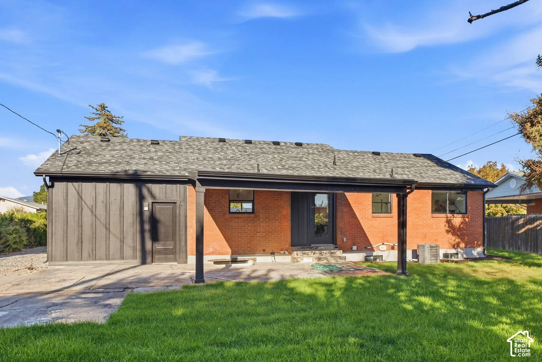 Brick exterior with a covered patio, garage with vertical siding, and a grass lawn