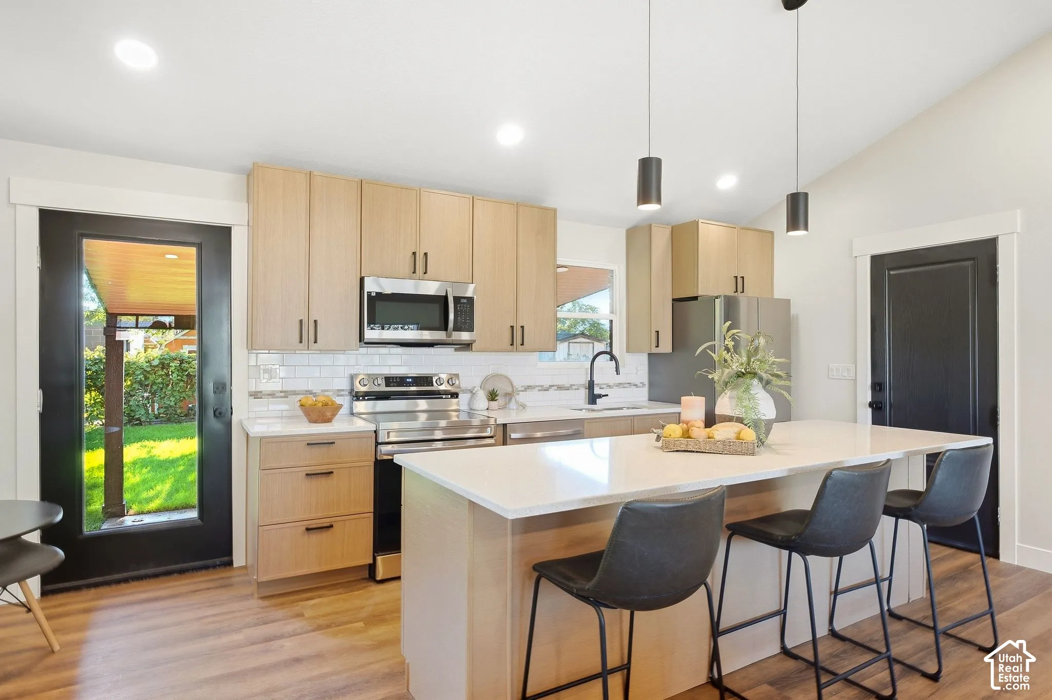 Vaulted ceiling, recessed lighting, wood-finish flooring, light wood cabinetry, and a kitchen island with seating