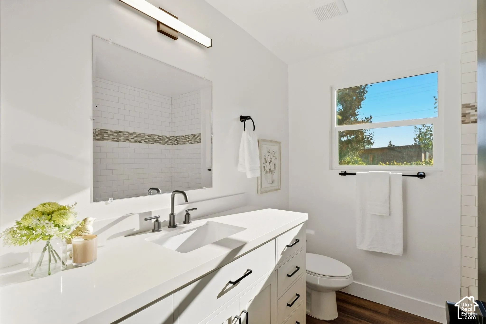 White vanity with integrated sink, dark bronze-finish fixtures, large frameless mirror, and a linear vanity light