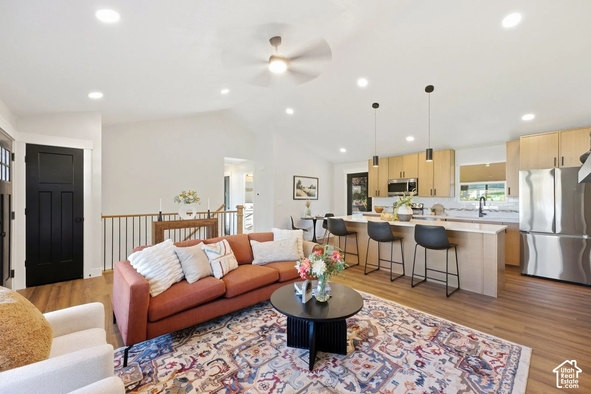 Open-concept living area featuring vaulted ceilings, recessed lighting, wood-finish flooring, a kitchen island with pendant lighting, and stainless steel appliances