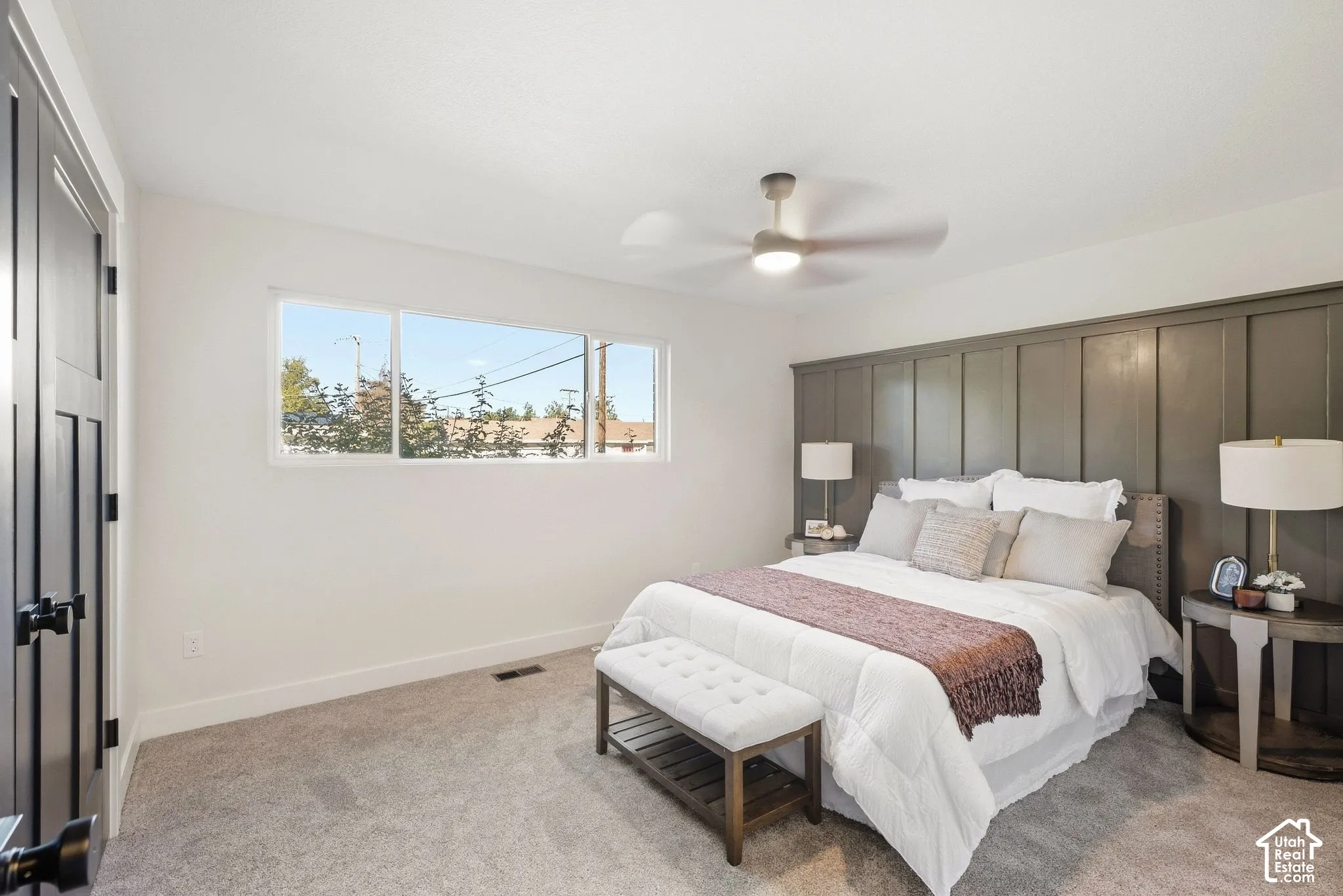 Wall-to-wall carpeted flooring, white painted walls, horizontal window array, ceiling fan with integrated light, and a feature wall with vertical paneling