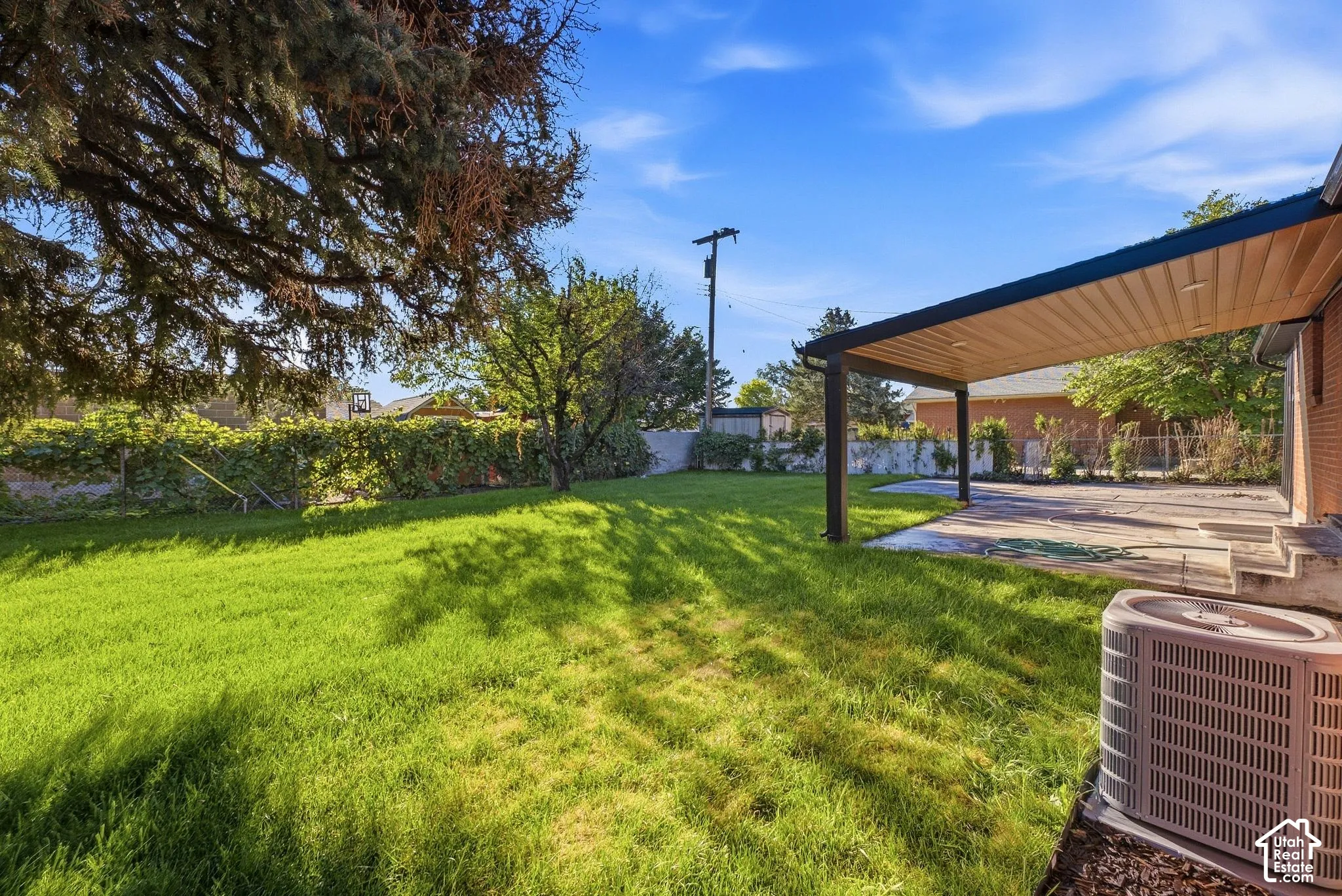 Expansive lawn with mature trees and a covered patio area, featuring a concrete surface and brick exterior