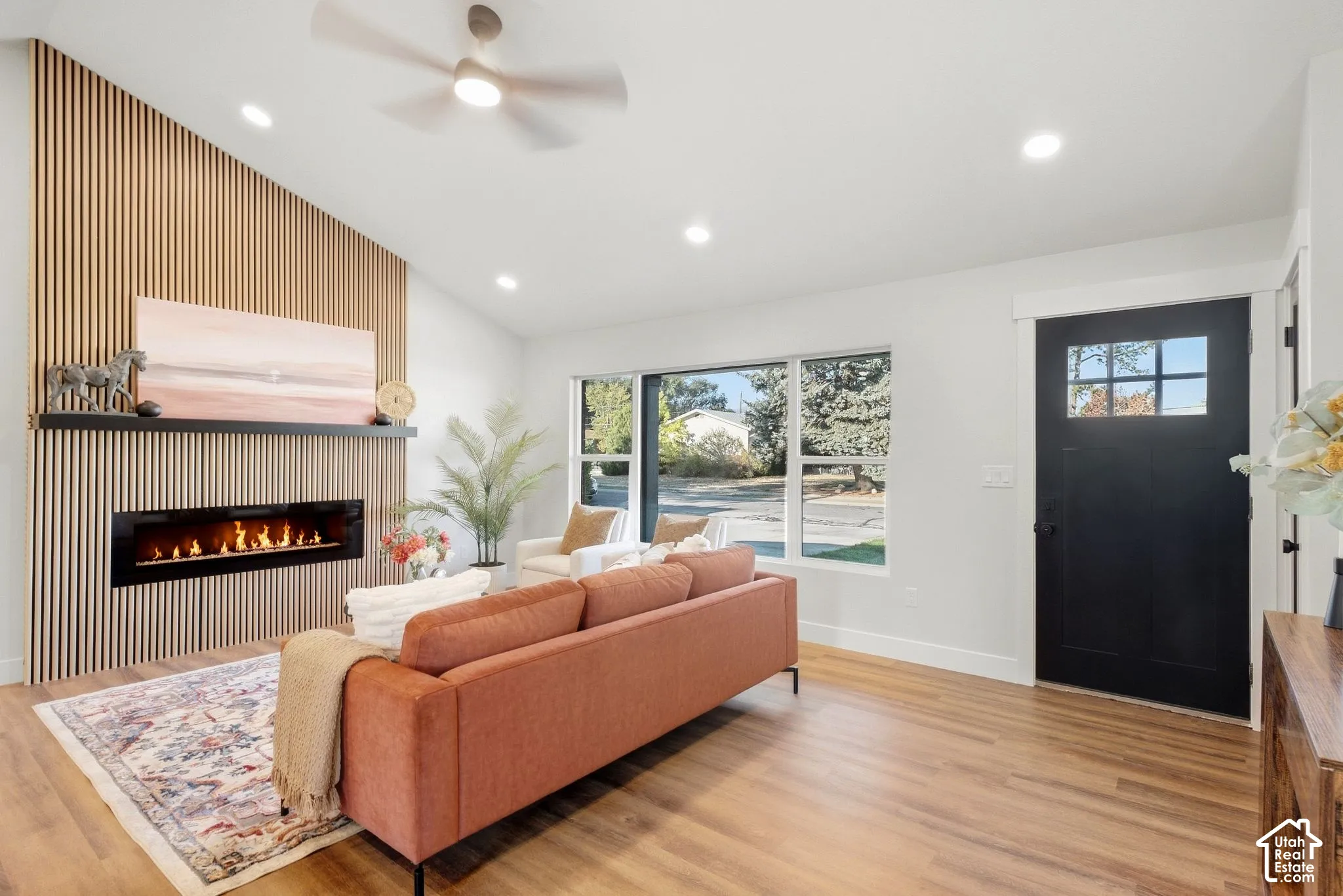 Vaulted ceiling with a ceiling fan, wall-mounted linear fireplace, wood-finish flooring, recessed lighting, and a front entry door with glass panels