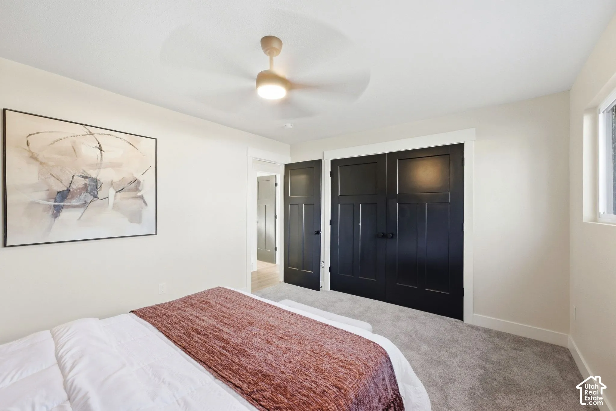 Plush carpet flooring, a ceiling fan with integrated lighting, a double-door closet with dark panel doors, and a window providing natural light