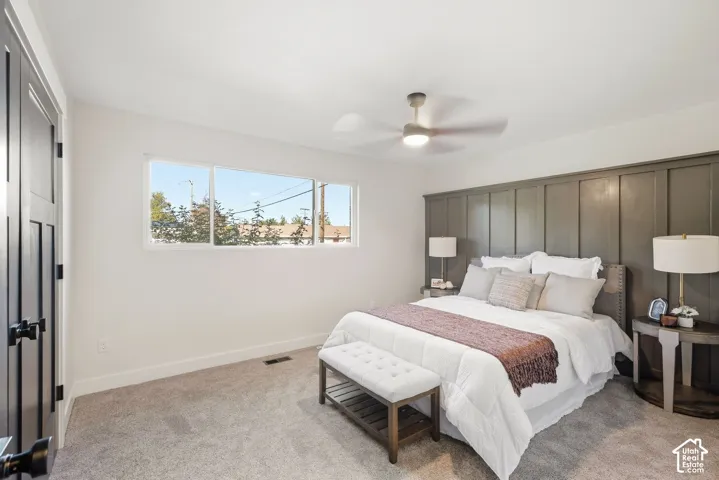 Wall-to-wall carpeted flooring, white painted walls, horizontal window array, ceiling fan with integrated light, and a feature wall with vertical paneling
