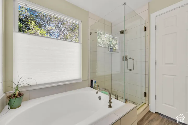 Soaking tub with brushed nickel fixtures, euro glass-enclosed shower, tiled shower surround, and natural light from window