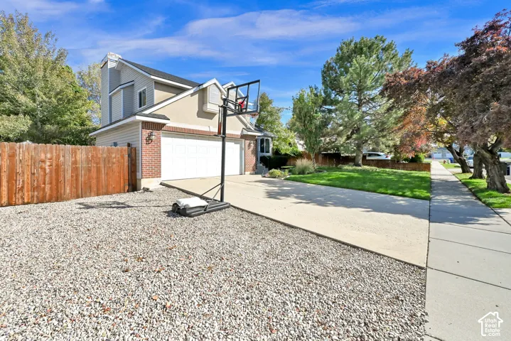 Brick and siding exterior, two-car garage, expansive paved driveway, mature trees, and a concrete sidewalk