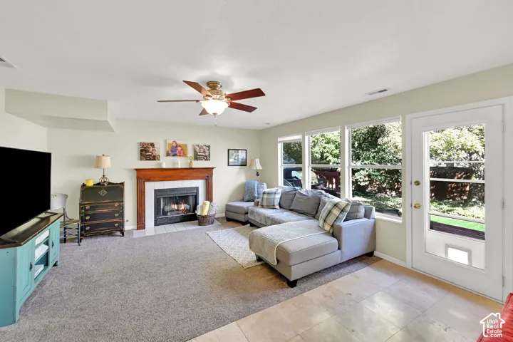 Living space featuring a fireplace with a wood mantle, a ceiling fan, multiple windows, a glass-paneled door, and mixed flooring