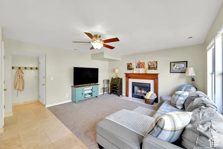 Built-in fireplace with wood mantel, ceiling fan with light fixture, carpeted flooring, tile entry, and large windows