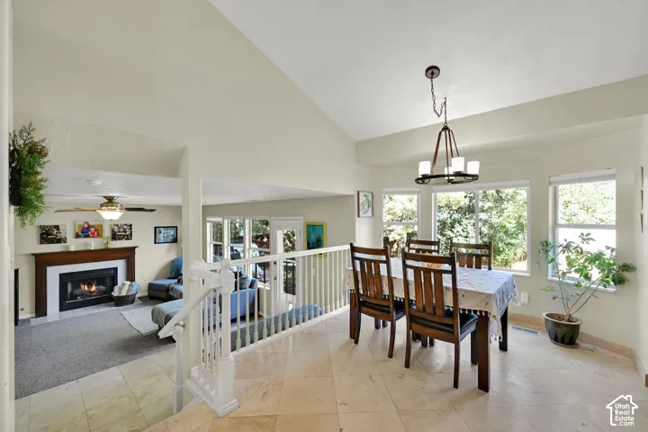 Vaulted ceiling with a chandelier, tile flooring, window grouping, white railings, and a fireplace with a wood mantel