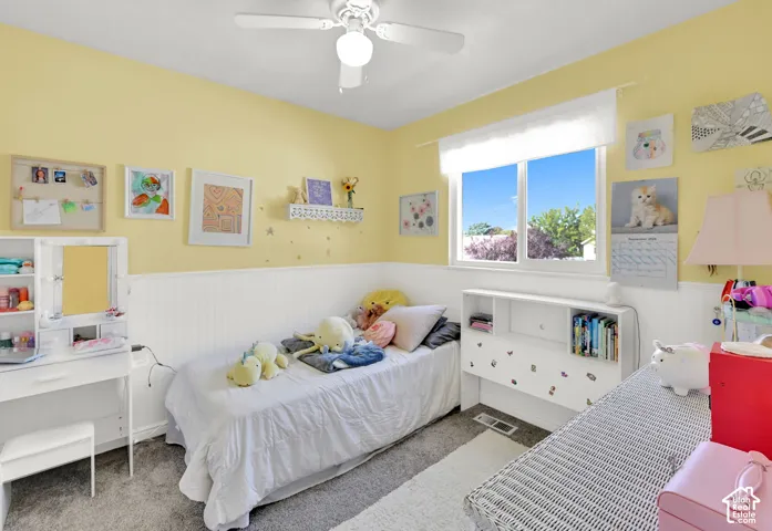 Wall-to-wall carpeting, bright window with white trim, white wainscoting, and a ceiling fan with light