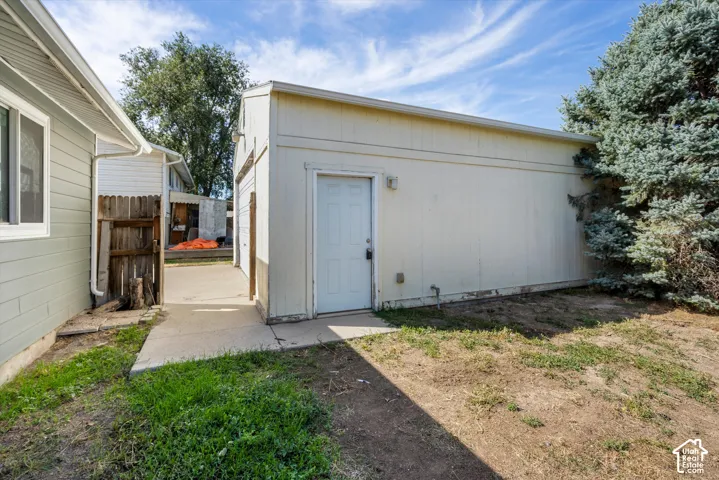 Detached structure with a side entry door, concrete pathway, and adjacent evergreen shrubbery