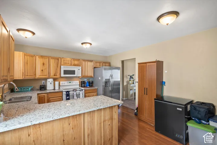 Kitchen featuring wood cabinetry, light-toned countertops, stainless steel refrigerator, and wood-finish flooring