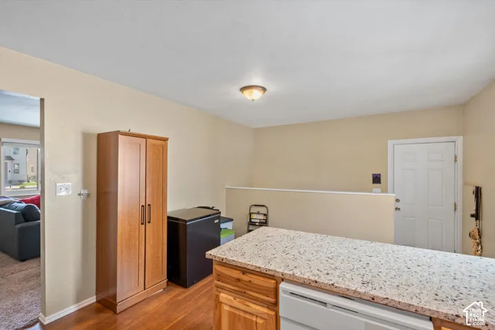 Kitchen island with speckled countertop, wood-finish cabinetry, and integrated dishwasher