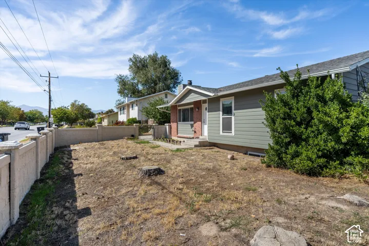 Light green siding exterior with a brick accent entry, concrete walkway, concrete perimeter wall, and established front yard shrubbery