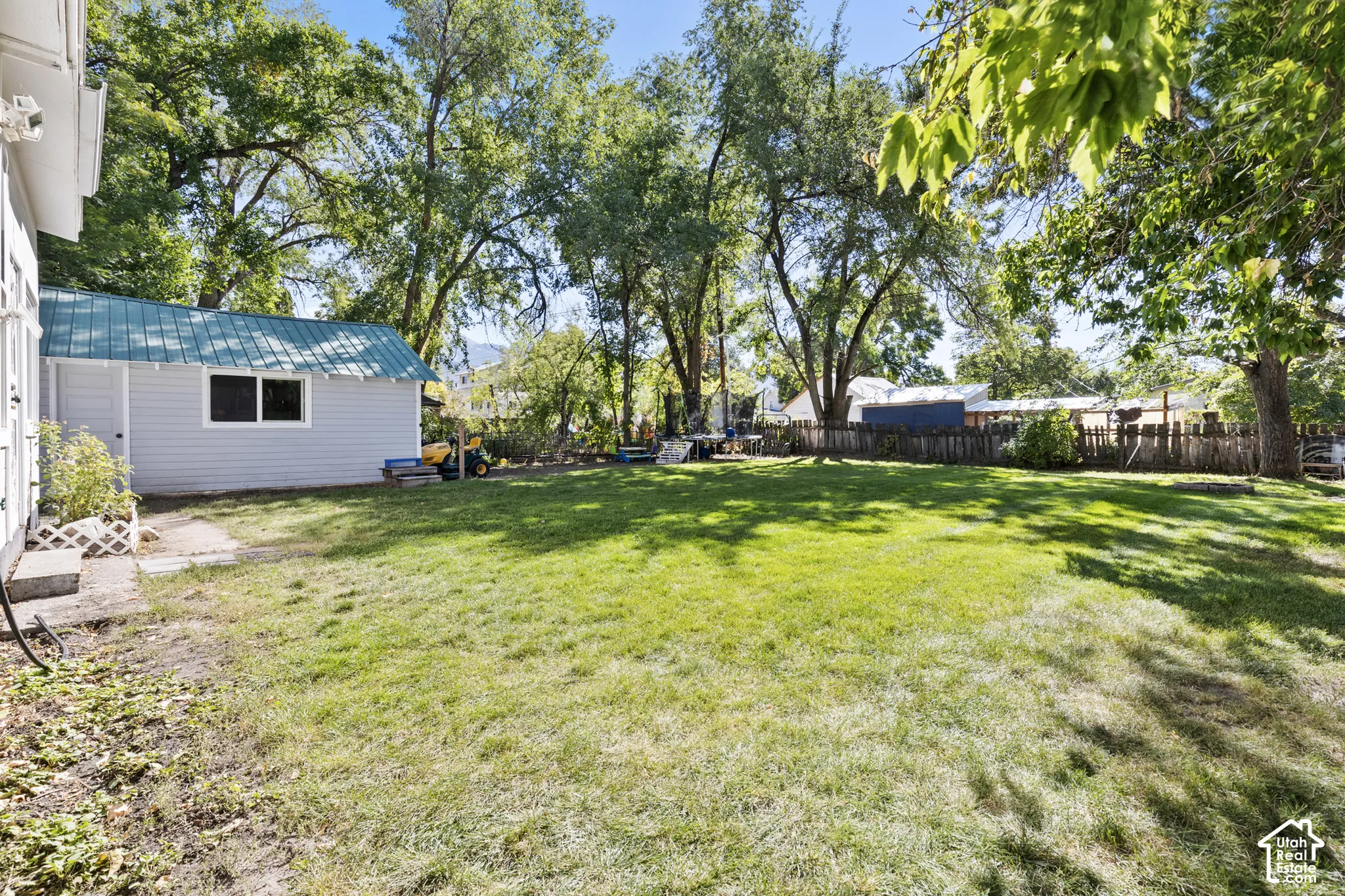 Shaded, fully fenced backyard & view of detached garage with metal roof.