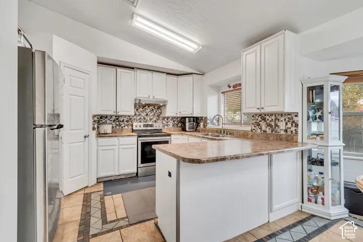 Kitchen featuring white cabinetry, stone-look countertops, a mosaic tile backsplash, stainless steel appliances, and tile flooring