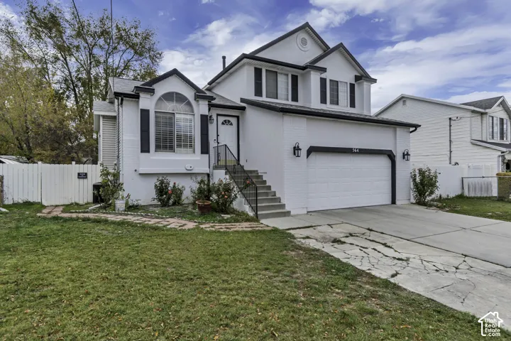White brick exterior, arched window detail, attached two-car garage, front entry staircase with metal railing, and a fenced side yard