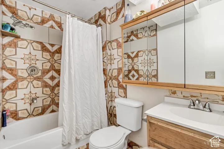 Bathroom featuring a built-in tub with a shower fixture, decorative tiled walls, a wood-finish vanity with an integrated sink, and a mirrored medicine cabinet