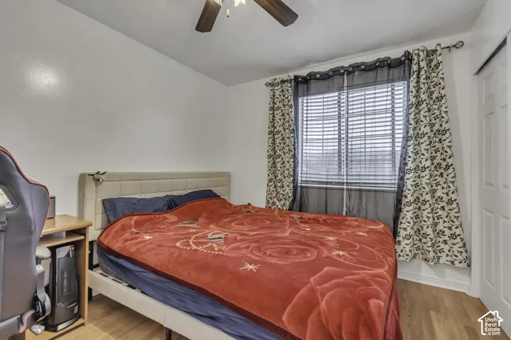 Wood-finish flooring, ceiling fan, window with blinds, and white paneled door