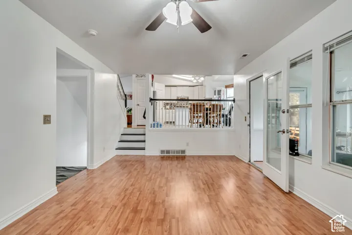 Wood-finish flooring, white walls, ceiling fan, glass-paned door, and staircase with dark treads