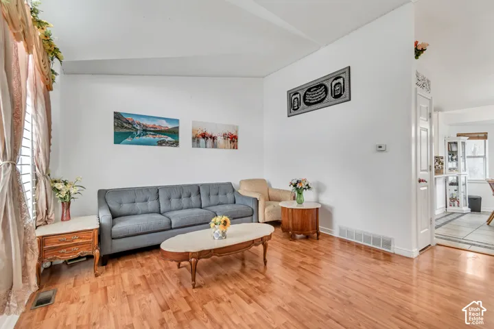 Vaulted ceiling, wood-finish flooring, white walls, and a window with vertical blinds