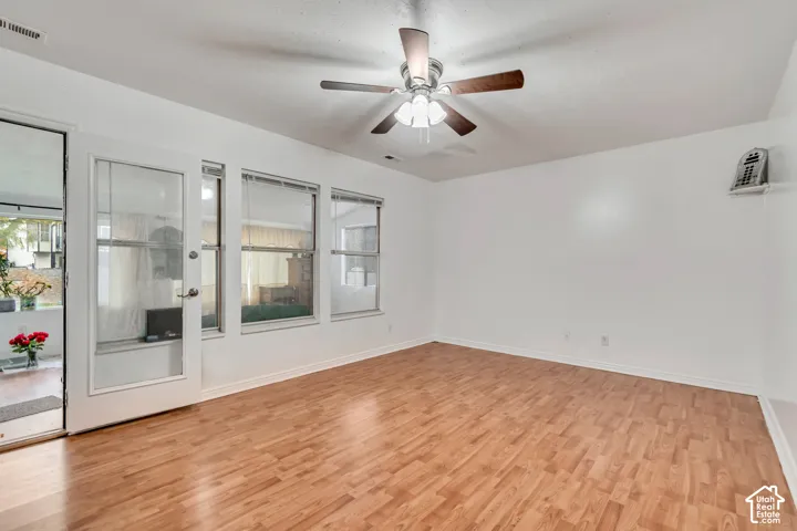 Wood-finish flooring, ceiling fan with integrated lighting, multiple windows providing natural illumination, and a glass-paneled door