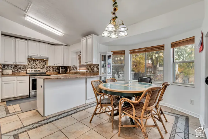 White cabinetry, patterned backsplash, light-toned countertops, and a bay window