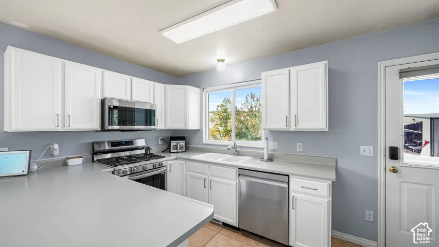 White cabinetry, stainless steel appliances, dual basin sink, light-toned countertops, and tiled flooring