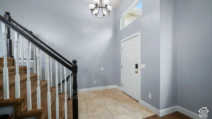 Tiled entryway flooring, carpeted staircase with white spindles and dark wood-finish handrail, and a decorative chandelier