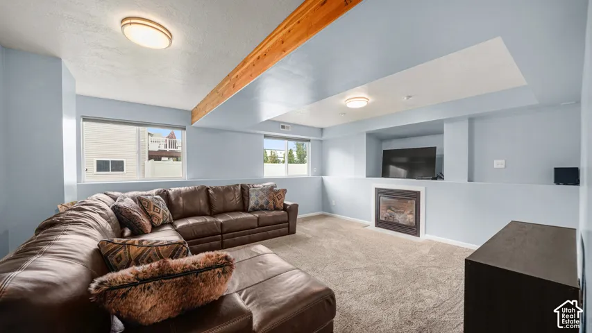 Recessed fireplace with a dark surround, carpet flooring, windows, and exposed ceiling beam