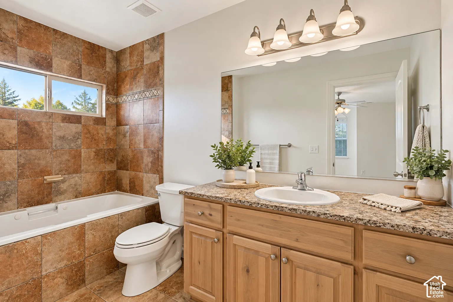 Built-in bathtub with tiled surround, dual windows, wood-finish vanity with an integrated sink, and a large wall-mounted mirror- VIRTUALLY STAGED