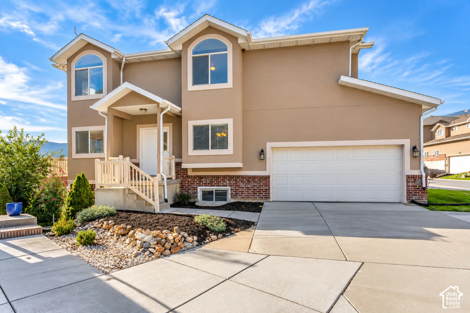 Stucco exterior with brick accents, arched windows, covered front entry, and an integrated two-car garage