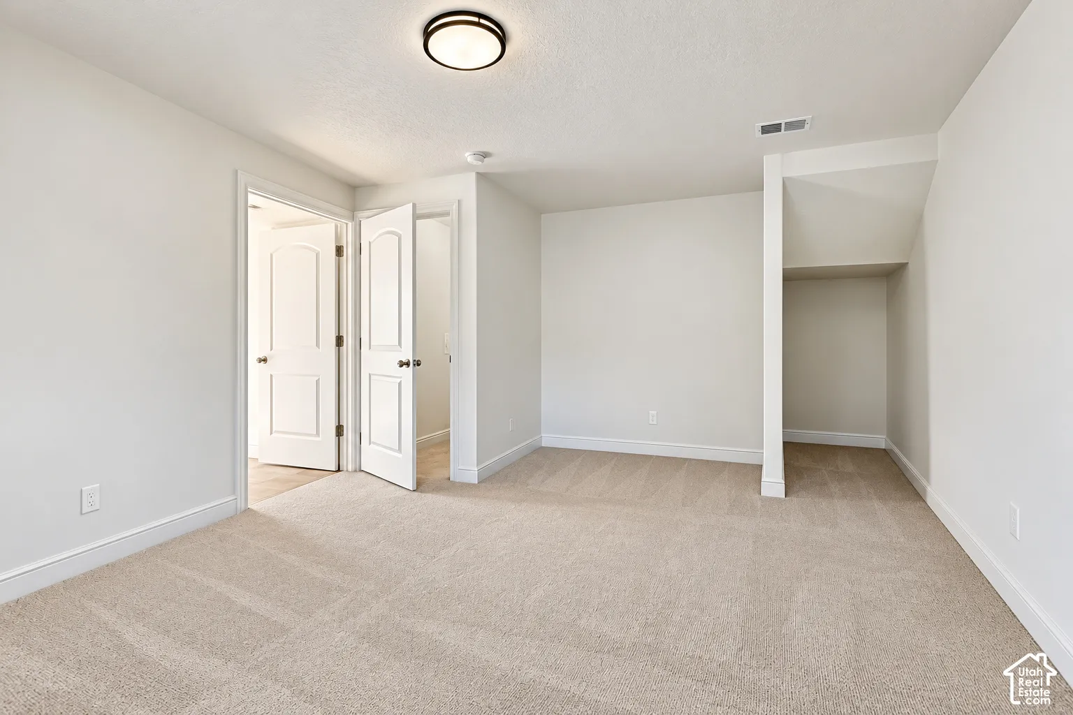 Neutral-toned carpeting, crisp white walls, flush-mount ceiling light fixture, and built-in alcove shelving