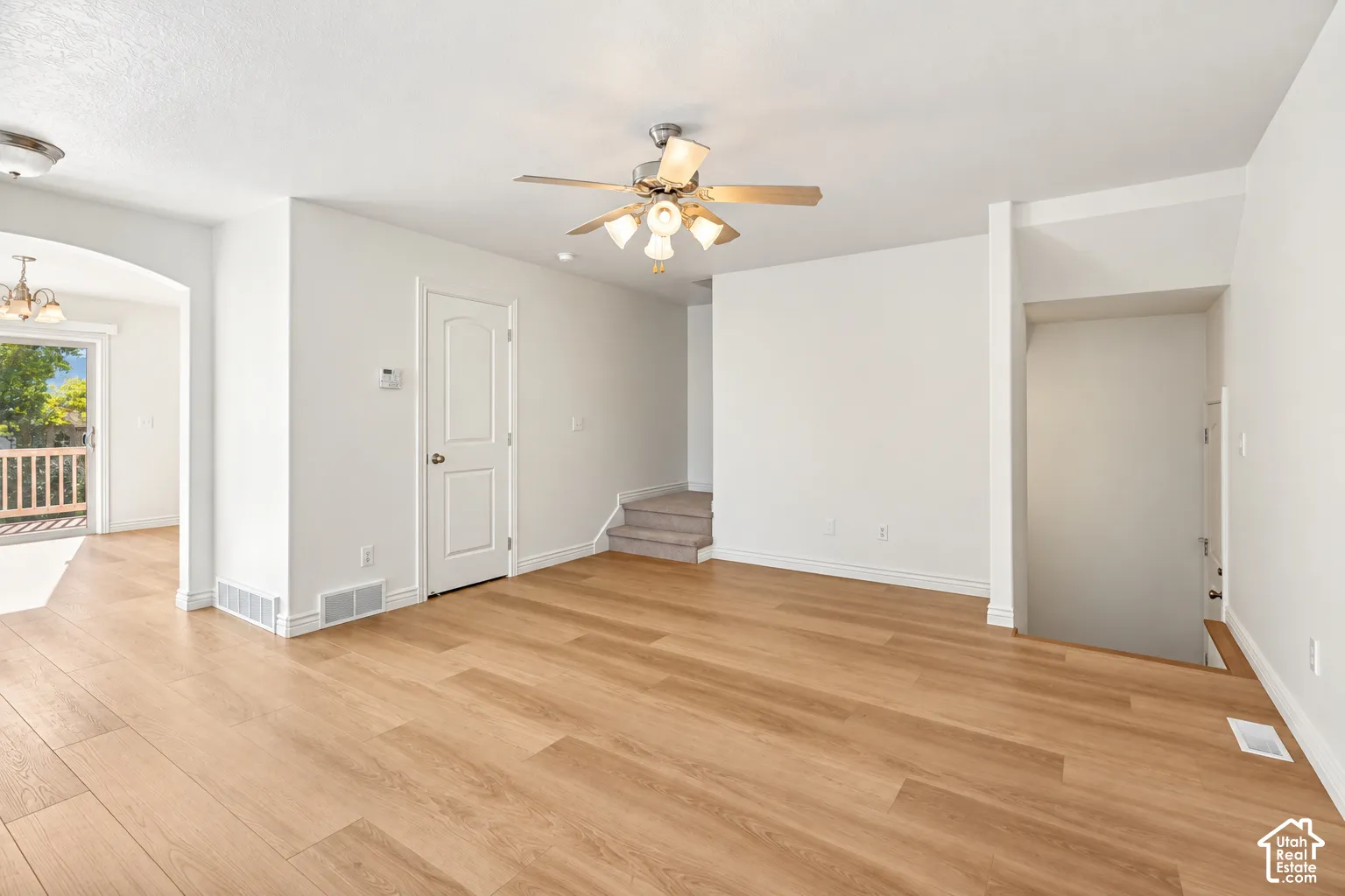 Wood-finish flooring throughout, ceiling fan with integrated lighting, and arched doorway leading to an outdoor deck