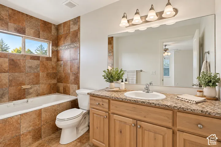 Built-in bathtub with tiled surround, dual windows, wood-finish vanity with an integrated sink, and a large wall-mounted mirror- VIRTUALLY STAGED