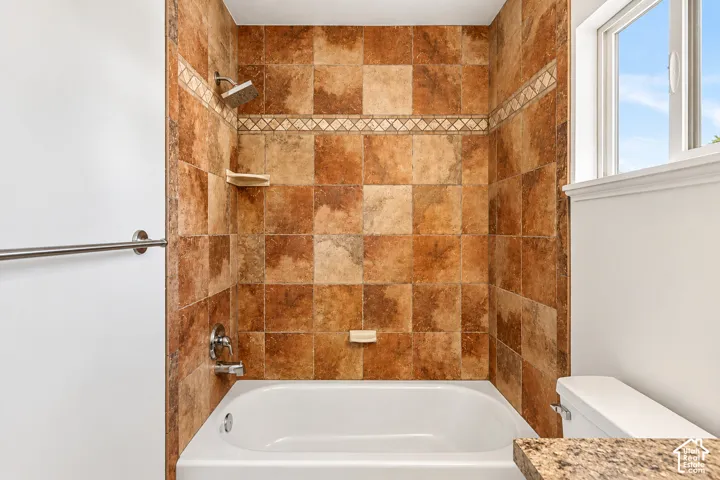 Bathtub and shower combination featuring earth-toned wall tile with an accent border, polished chrome fixtures, and a window
