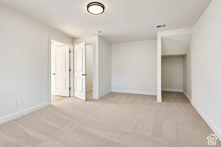 Neutral-toned carpeting, crisp white walls, flush-mount ceiling light fixture, and built-in alcove shelving