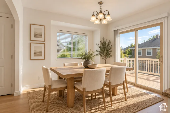Dining area featuring a bronze chandelier, wood-finish flooring, and direct access to an outdoor deck through a sliding glass door - VIRTUALLY STAGED