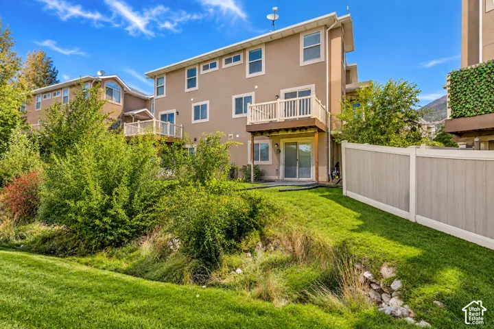 Stucco exterior featuring multiple windows, an upper-level deck, a lower-level patio with sliding glass doors, and a partial privacy fence