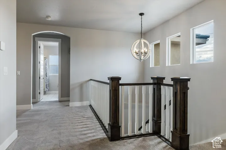 Carpeted hallway with an arched doorway, wood-finish and white baluster railing, and a decorative pendant light fixture