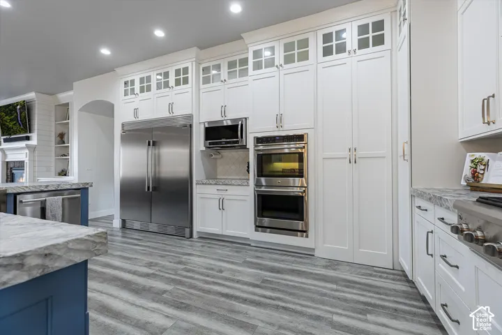 White shaker cabinetry with varied hardware, stainless steel appliances, wood-finish flooring, and light-toned countertops
