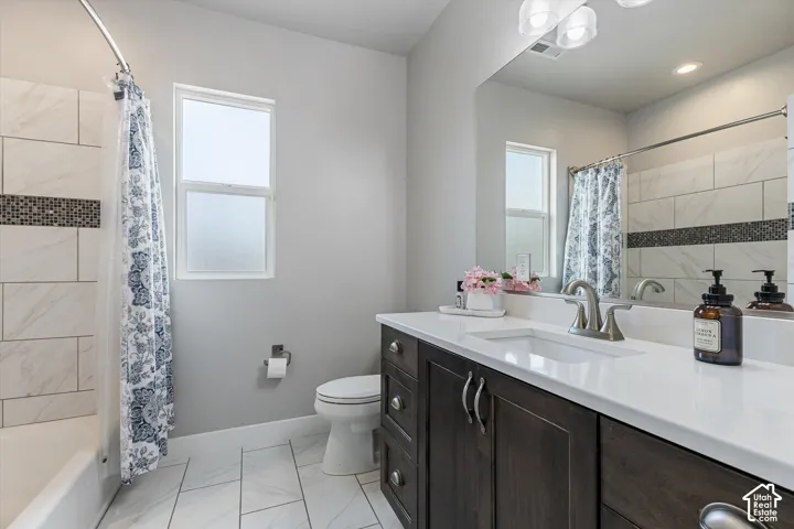 White tile flooring, dark wood-finish vanity with dual sinks, white countertop, white subway tile shower surround, and a frosted window