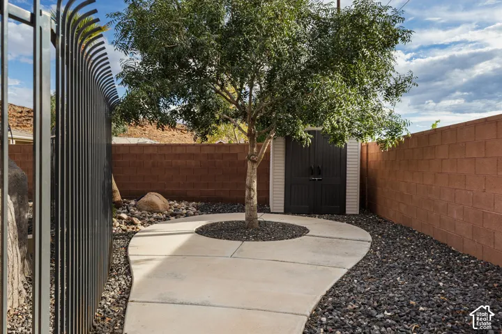 Winding concrete path, mature tree, well-defined landscaping, detached storage shed, and a privacy wall