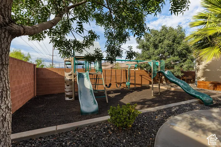 Landscaped backyard featuring a built-in play structure with slides and swings