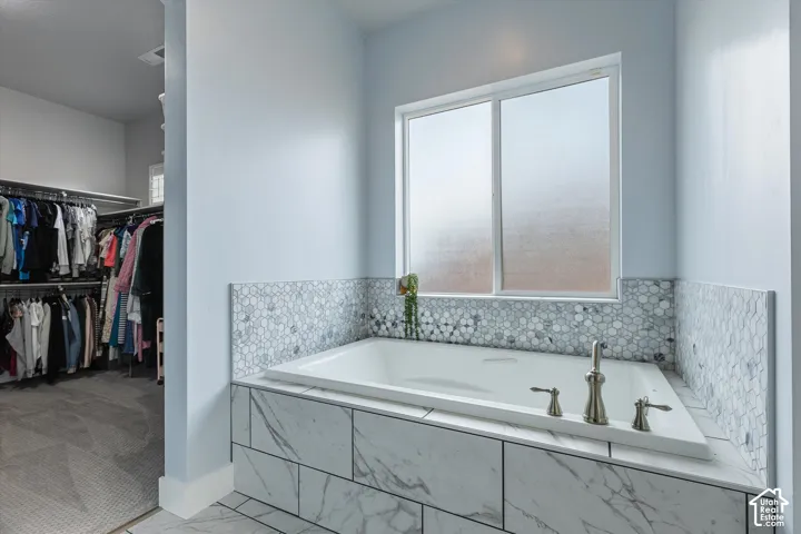 Soaking tub with brushed nickel fixtures, marble-look tile surround, and hexagonal mosaic wall tile